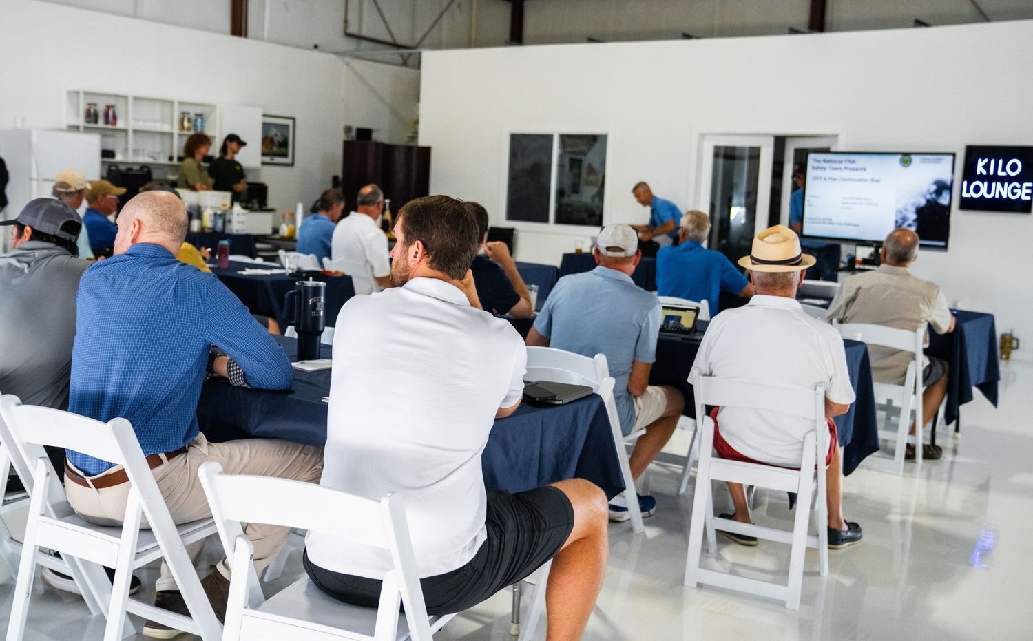Panoramic view of a meeting space with white chairs and presentation screens in a warehouse setting.