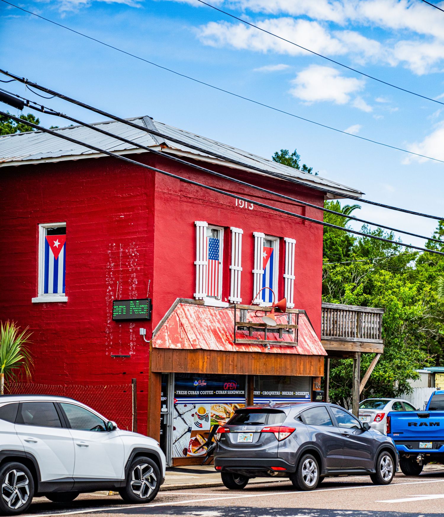 Bright red corner building with Cuban flag details and parked cars on a sunny day.