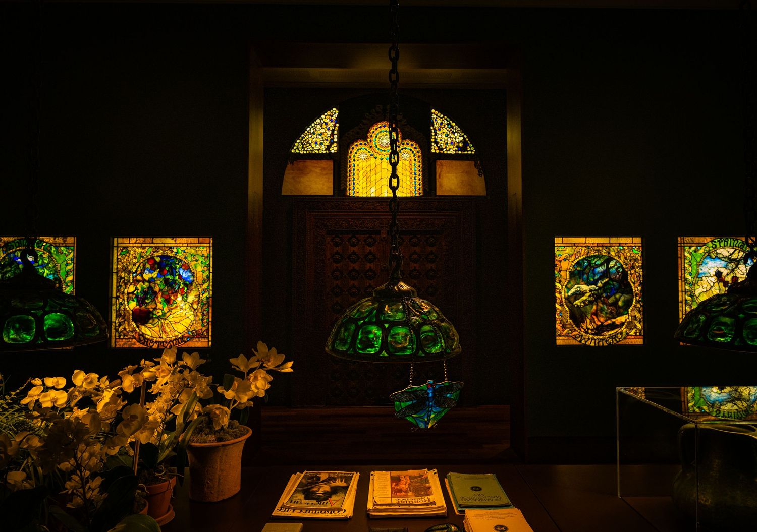 Museum gallery displaying multiple illuminated stained glass panels mounted on dark walls.