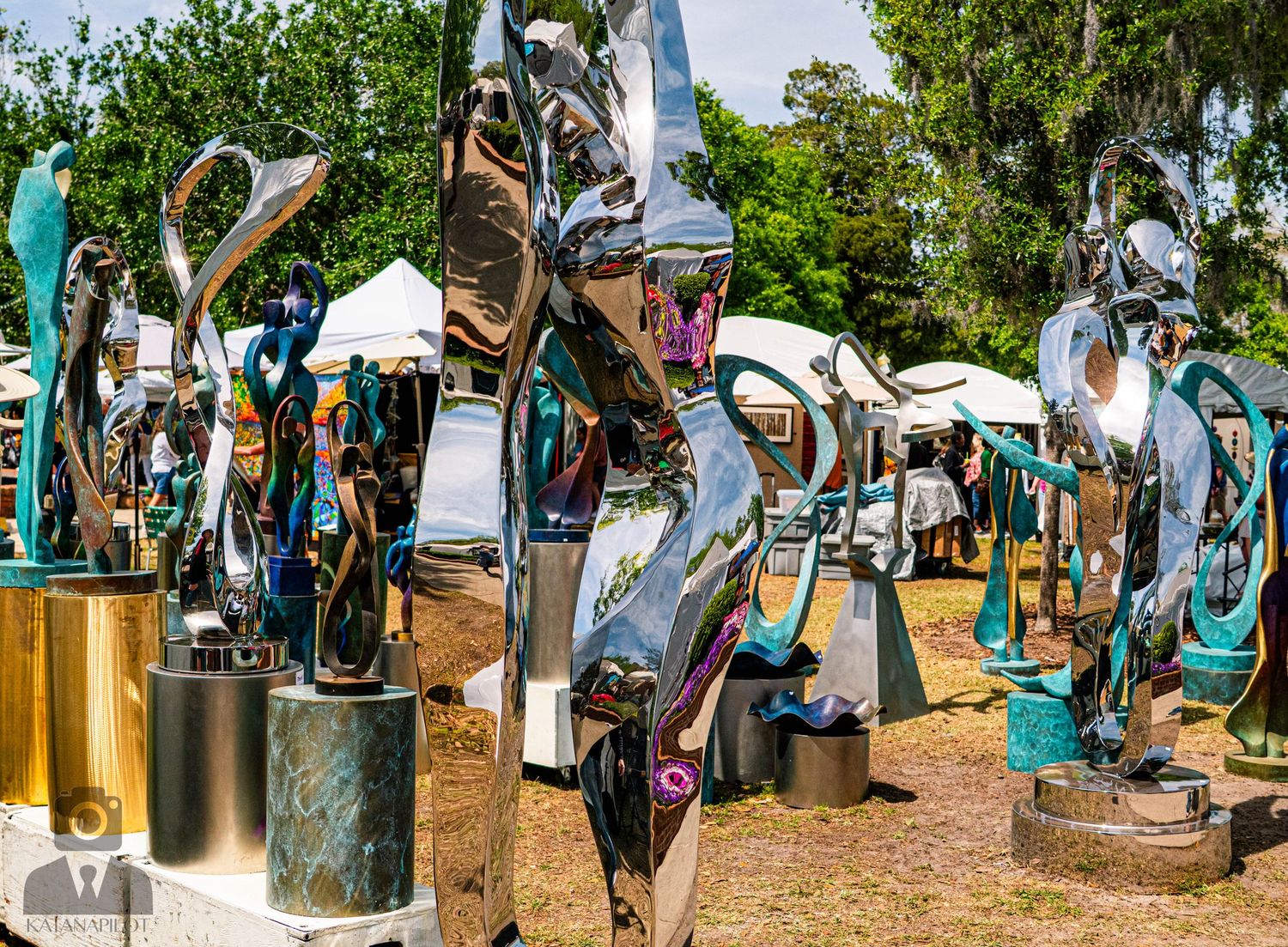 Outdoor festival scene with green trees and white tents lined up along a path.