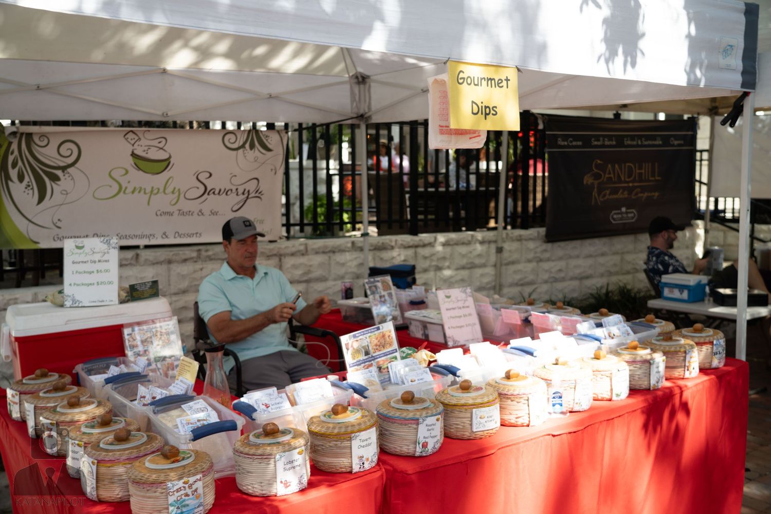 Market vendor displaying variety of packaged snacks and treats on red tablecloth.