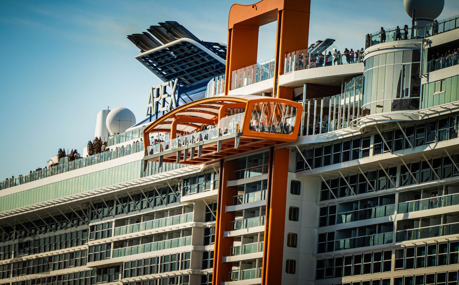 Solar panels and orange mechanical equipment mounted on the top deck of a modern cruise ship.