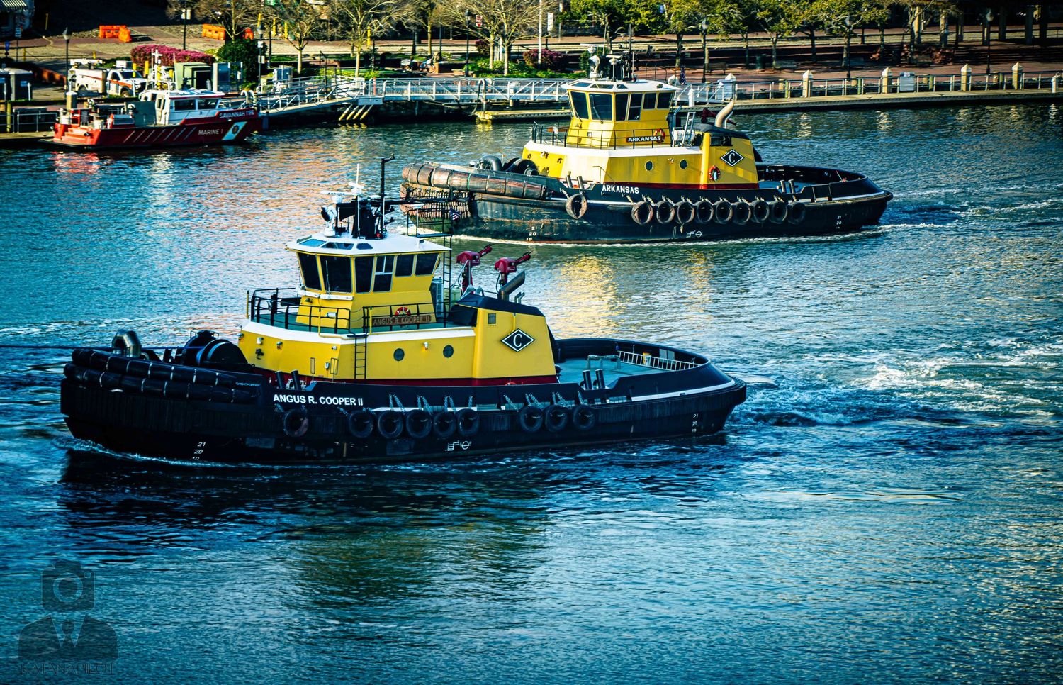 A fleet of tugboats and pilot boats navigate through blue harbor waters on a sunny day.