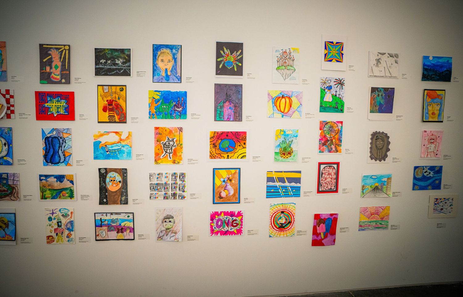 A wall display of colorful children's artwork featuring various drawings and paintings arranged in a grid pattern.