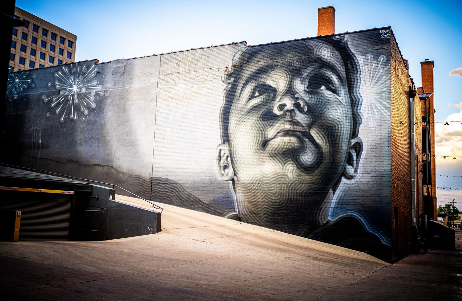 Large black and white mural of a child looking up at fireworks painted on a building exterior in an urban setting.