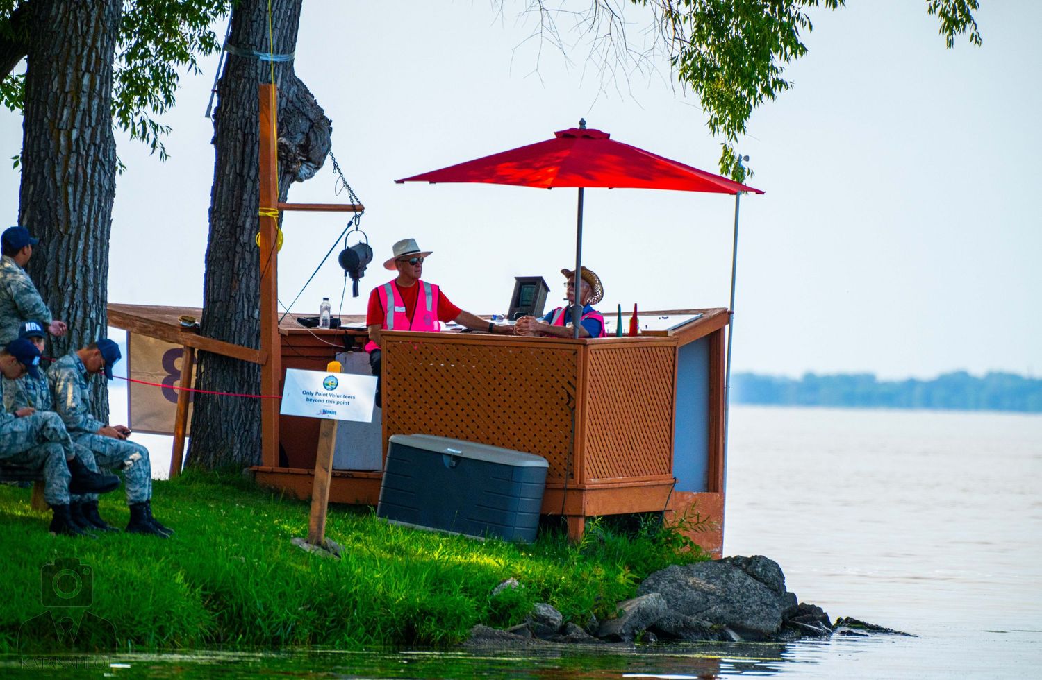 Lakeside concession stand with red umbrella serves customers on a sunny day.