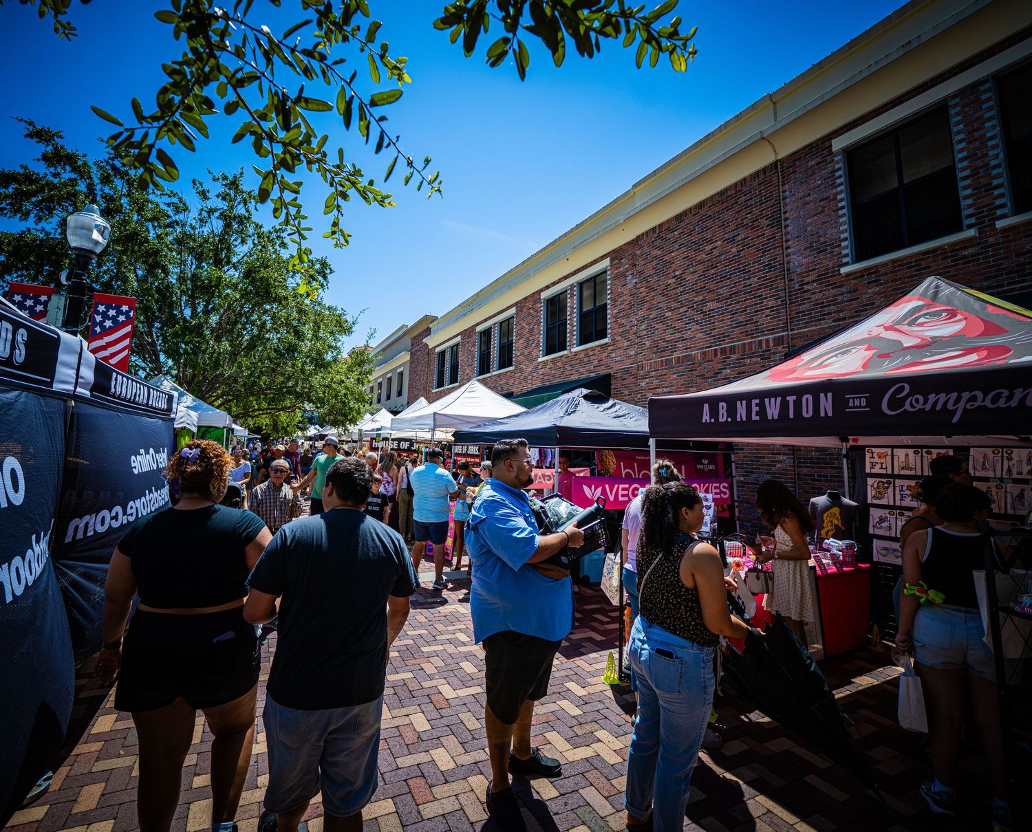 Outdoor vendor tents and crowds at a street festival outside brick buildings.