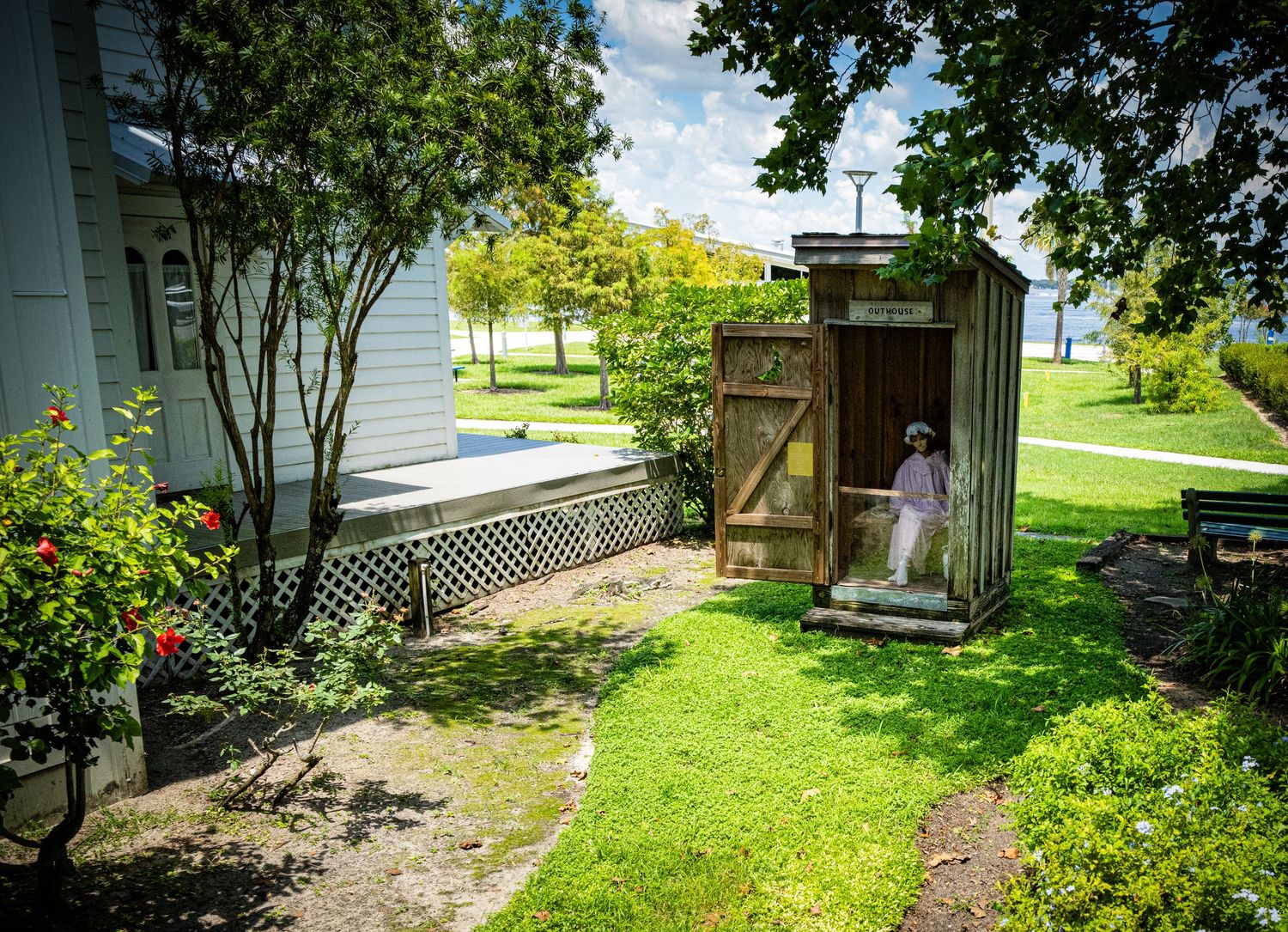 White wooden outhouse next to a historic house with green lawn and garden path.