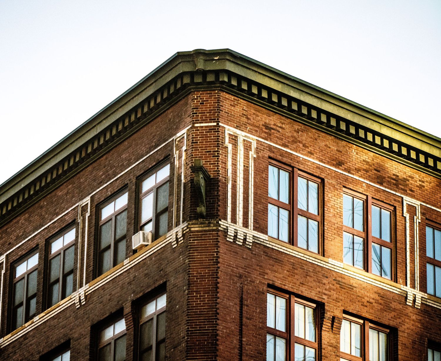Brick building exterior with repeating windows and architectural details in warm sunlight.