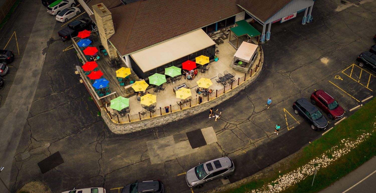 Overhead view of colorful market stalls and parked vehicles near a waterfront.