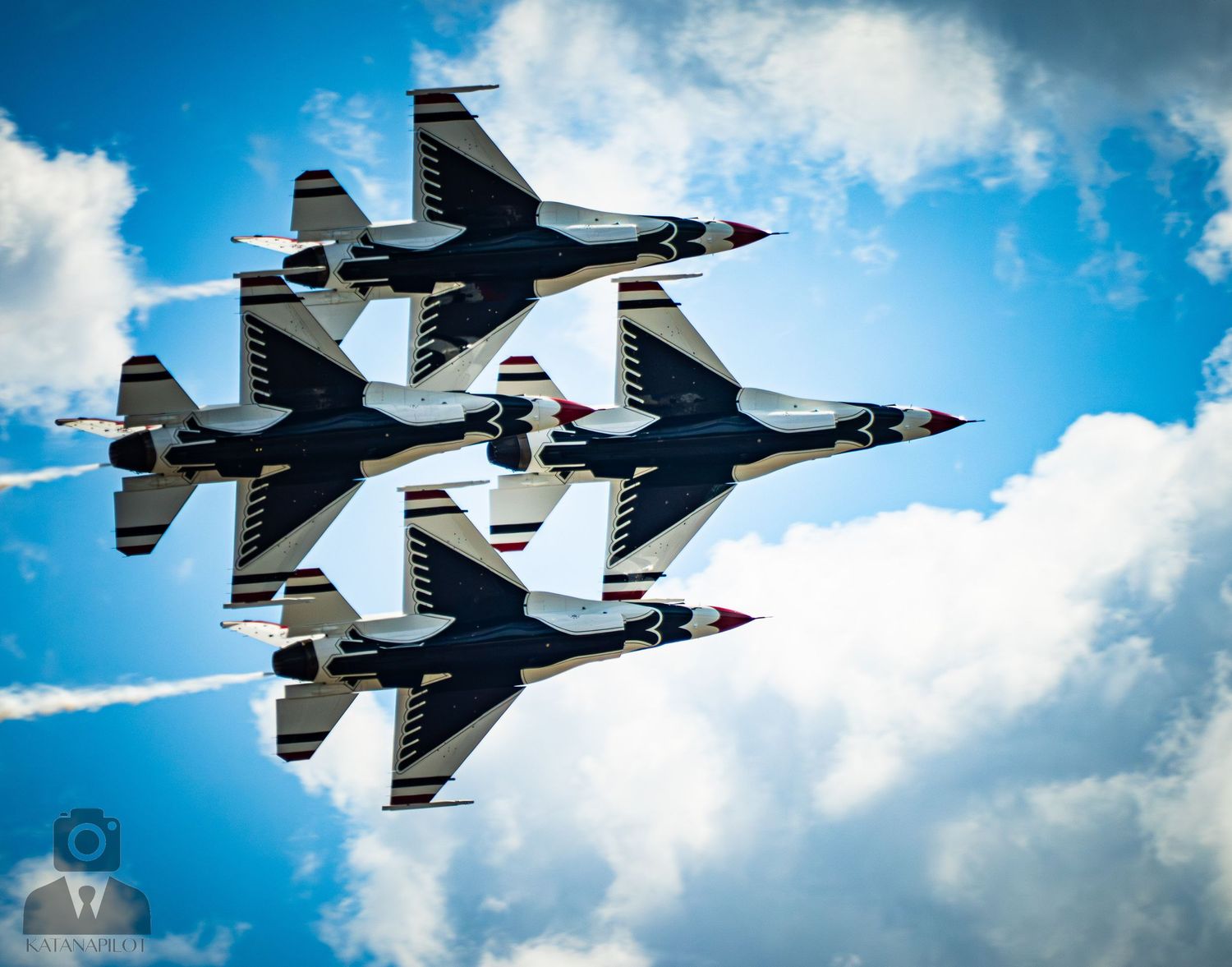 Four USAF Thunderbirds F-16 jets fly in tight diamond formation against a blue cloudy sky.