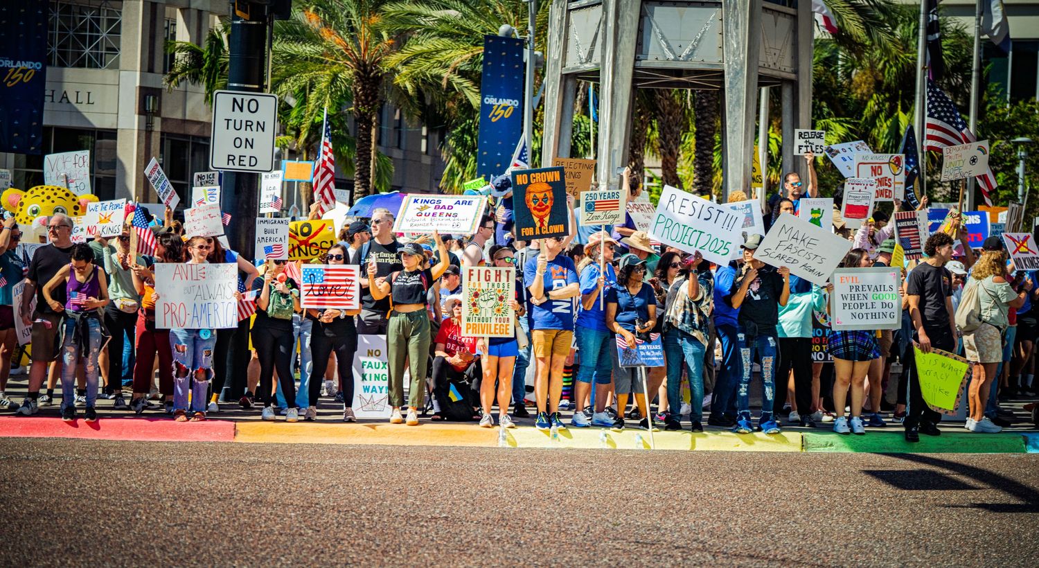 Long line of demonstrators with signs stretches down a palm tree-lined urban street.