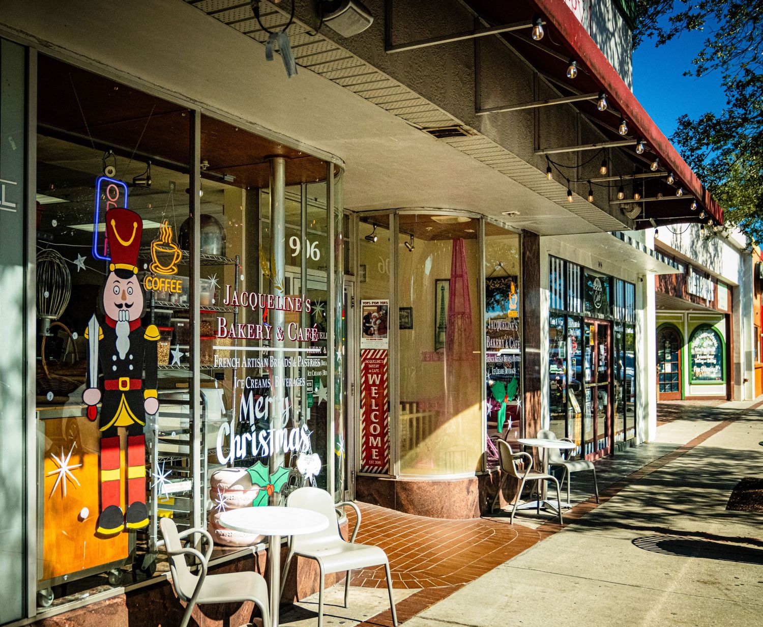 Small storefront windows display colorful signs and posters along a covered sidewalk in a commercial district.