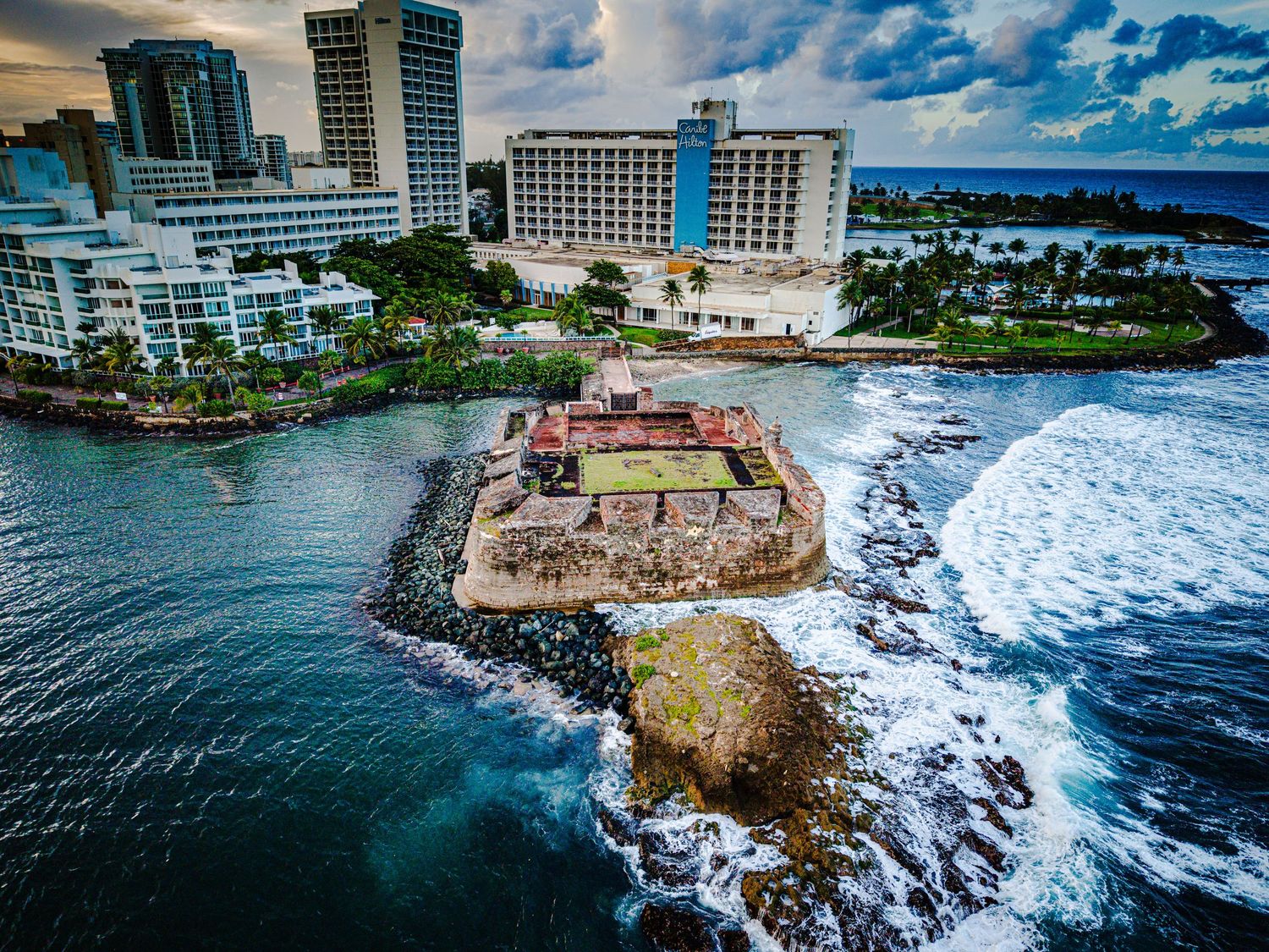 Dramatic coastal landscape showing high-rise hotels and rocky cliffs meeting the crashing waves of the Pacific Ocean.