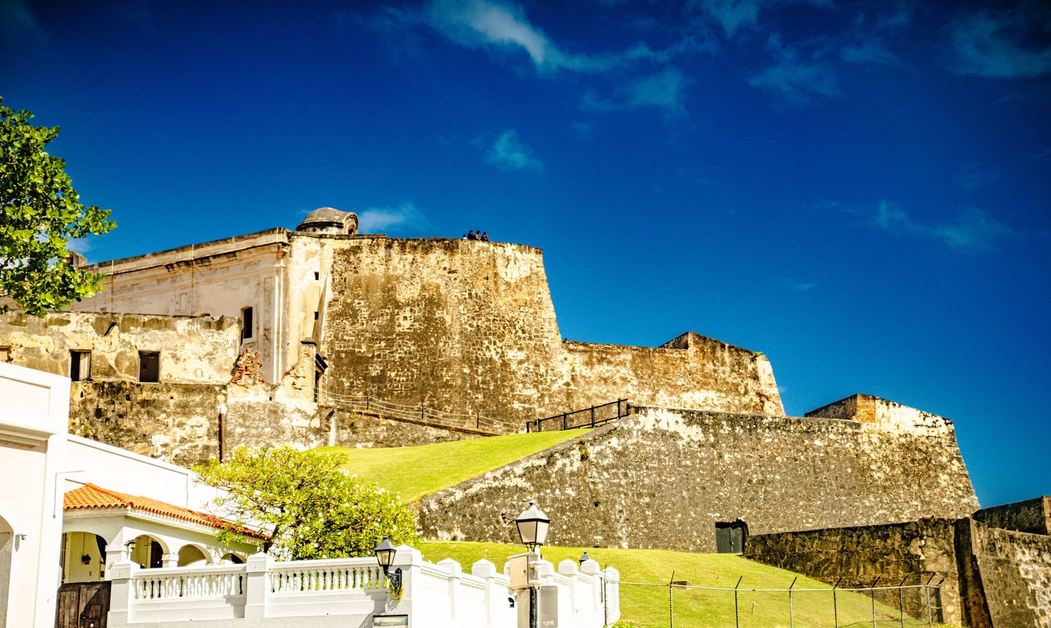Historic stone fortress walls and ramparts overlooking a coastal town under bright blue Caribbean skies.