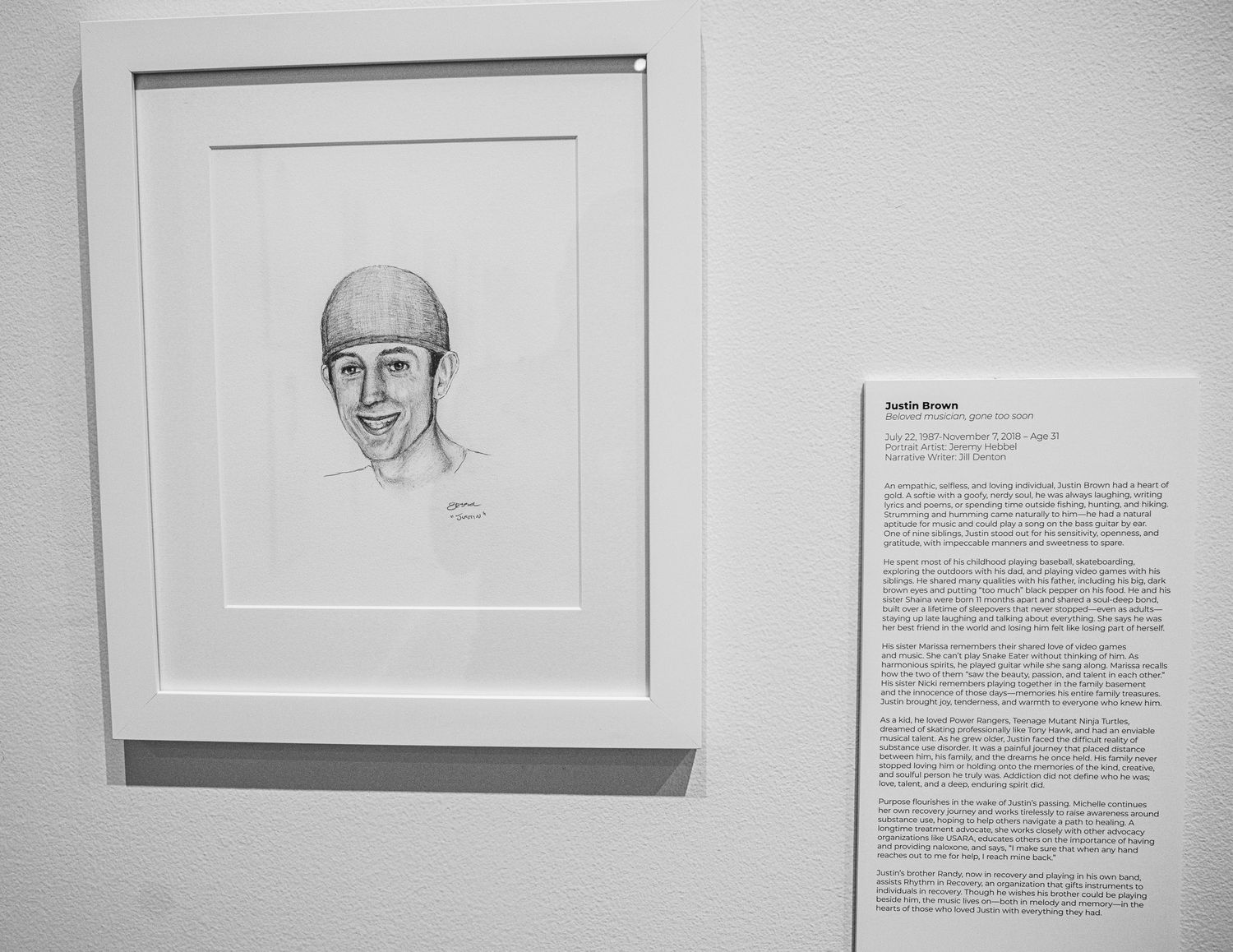 Exhibition wall showing framed portrait drawings alongside descriptive text panels.