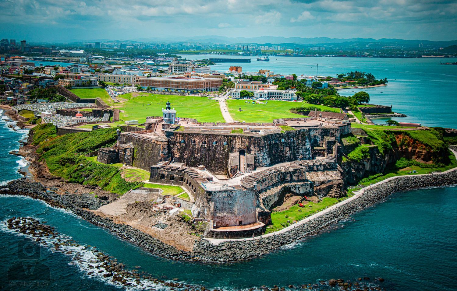 Dramatic aerial view of an ancient fortress perched on a rocky coastline with blue waters and green grounds.