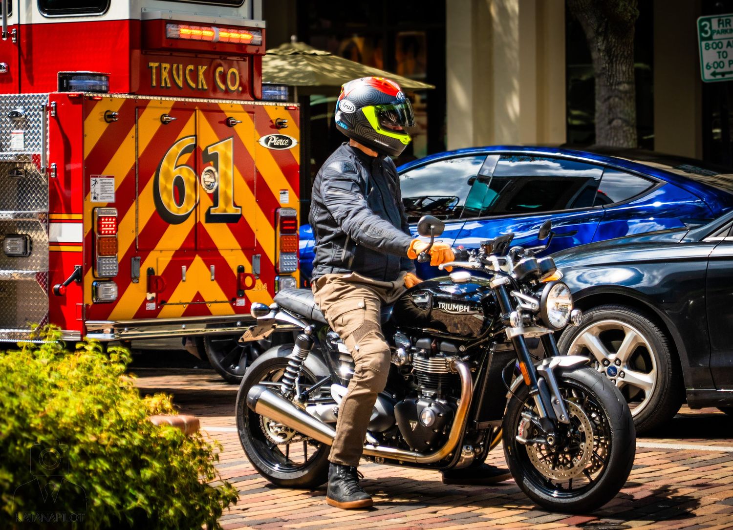 Red fire trucks and emergency vehicles are parked alongside a blue motorcycle on a brick street.
