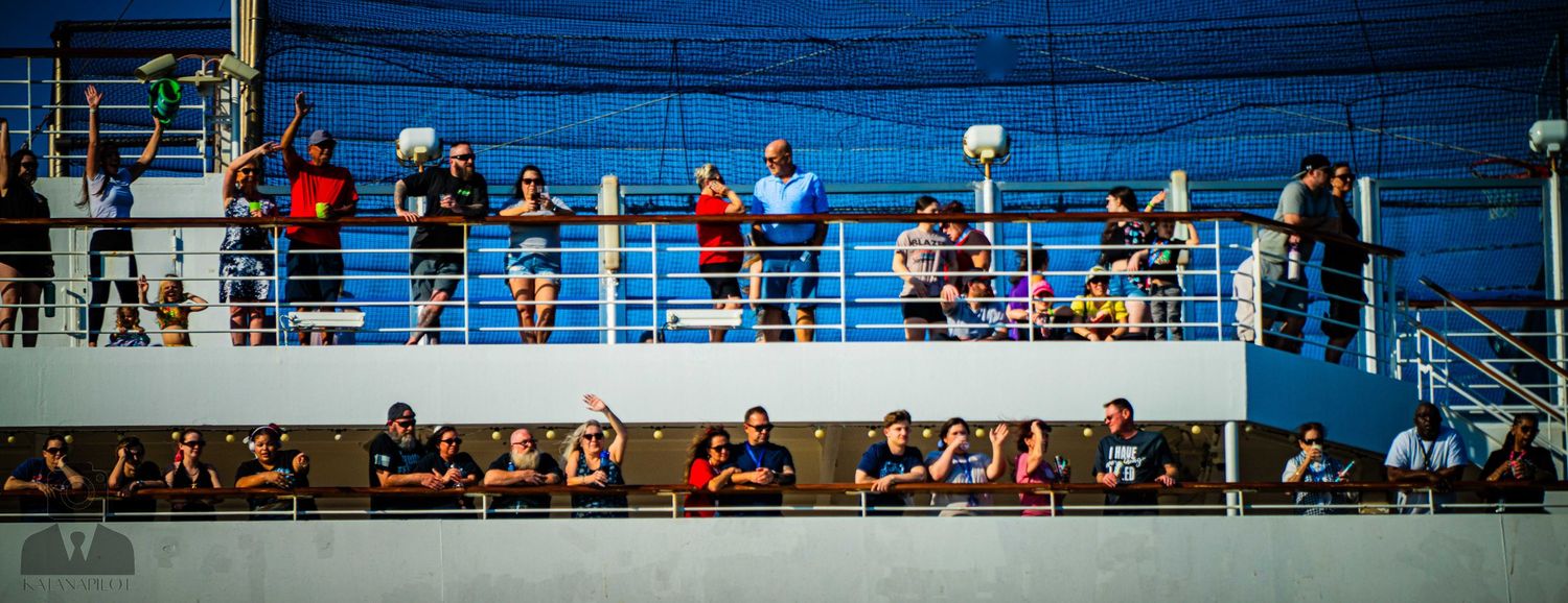 Spectators watch from bleachers overlooking a blue athletic field or sports facility during an outdoor event.