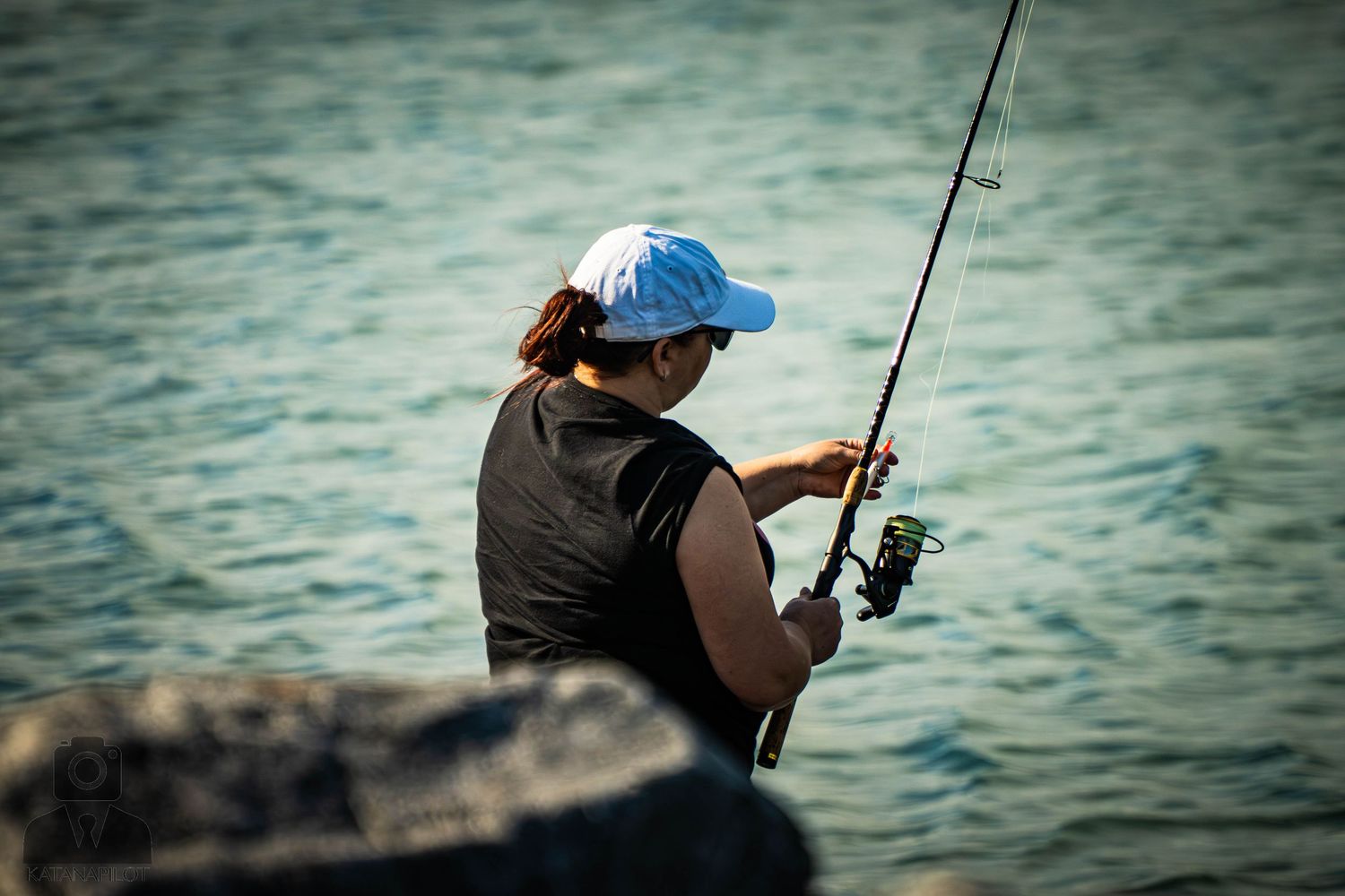 Close-up silhouettes of people fishing along a waterfront during sunset or sunrise.