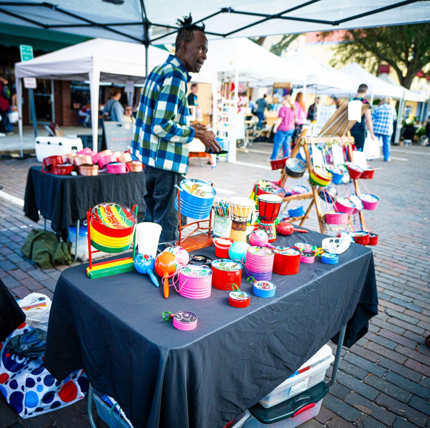 Colorful handmade singing bowls and meditation tools displayed on black tablecloth at outdoor market vendor stall.