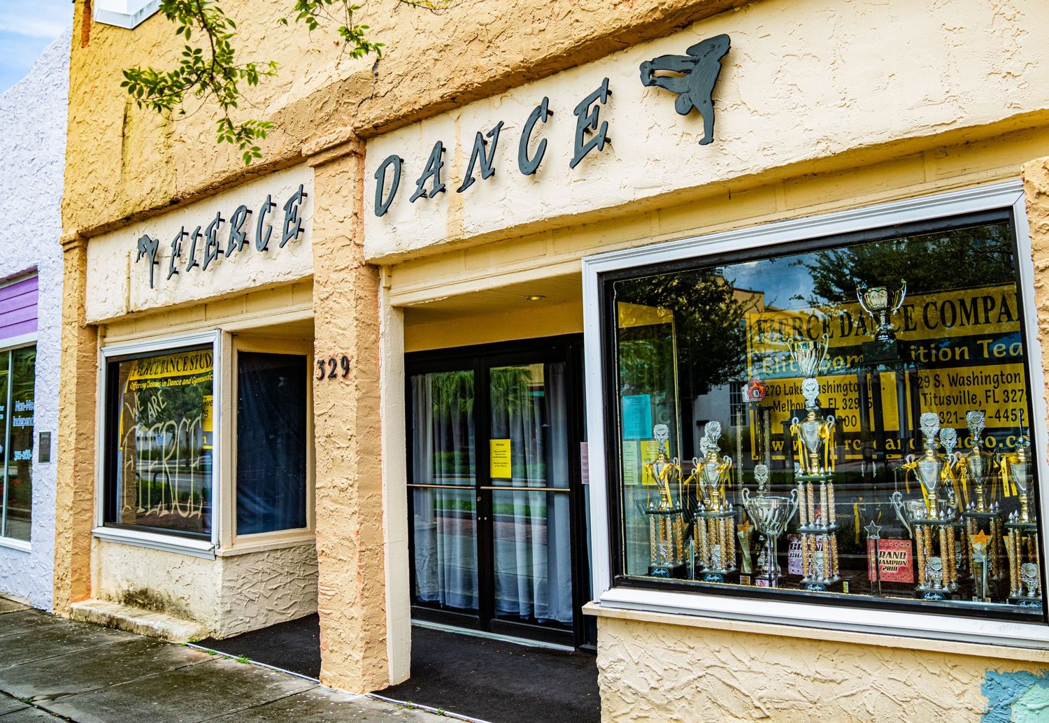 Exterior view of a strip mall with beige stucco walls and large storefront windows.