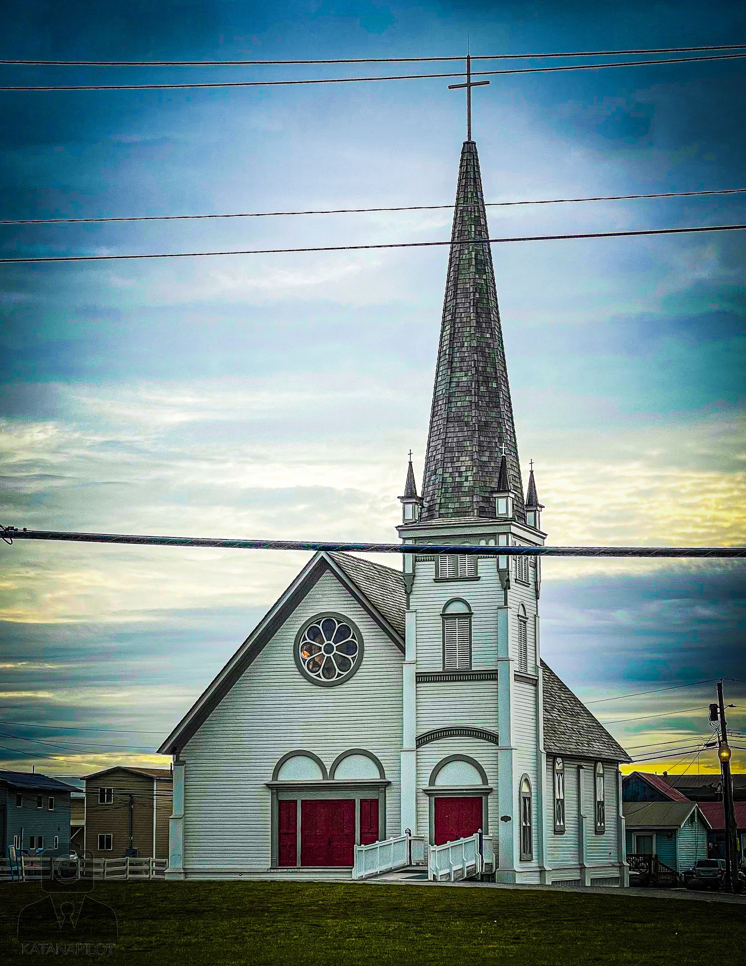 White wooden church with tall spire and clock tower against vibrant blue sky.