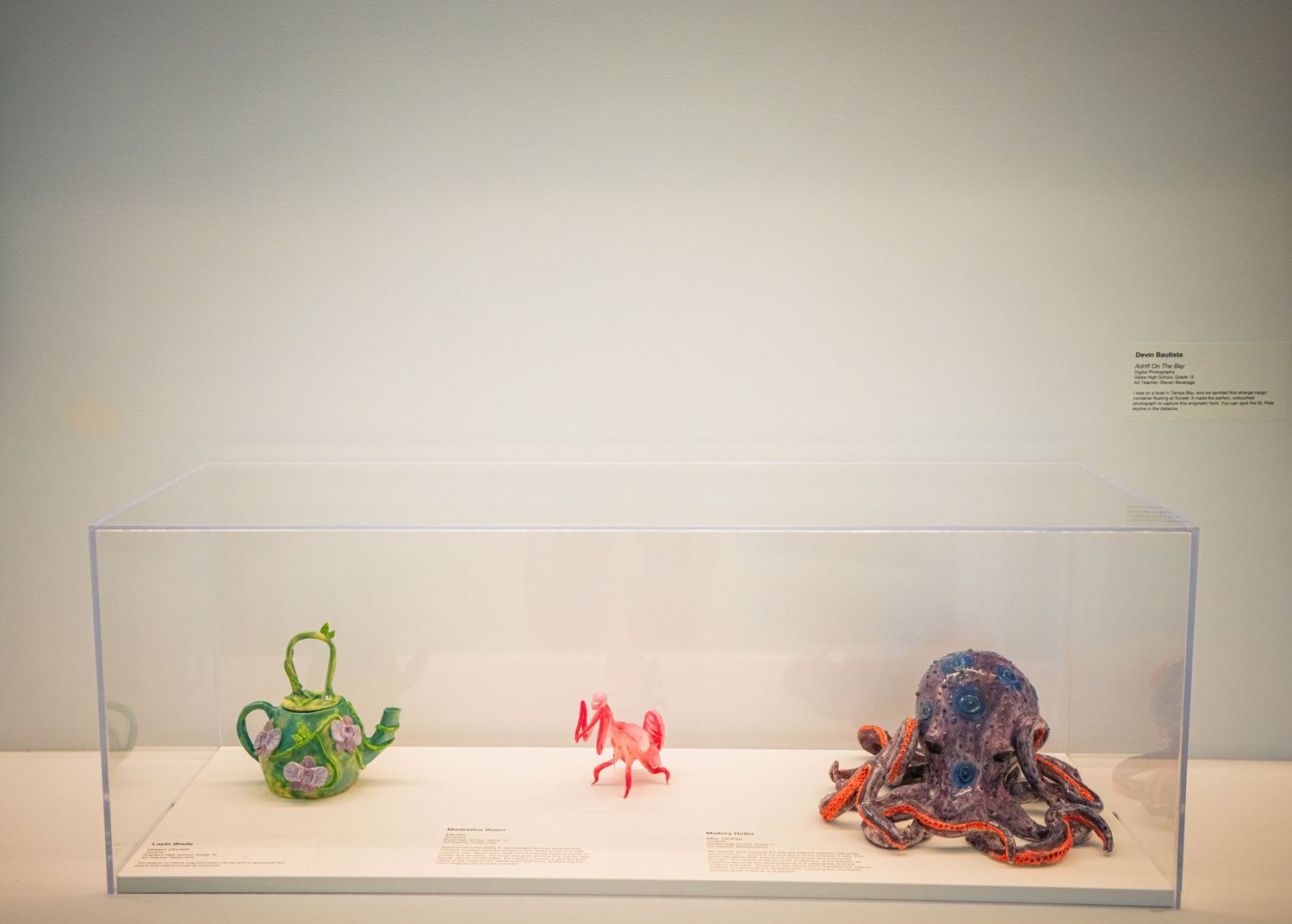 Small sculptures and art pieces displayed on white pedestals in a minimalist gallery setting.