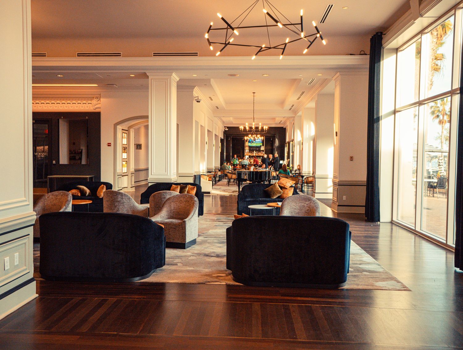 Modern open concept office space with dark hardwood floors, white walls, and large windows providing natural light.