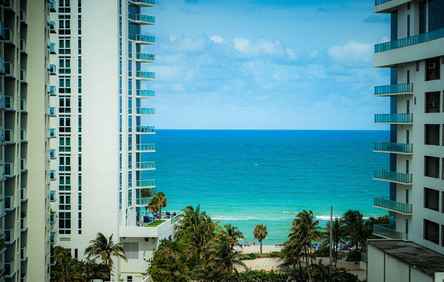 Panoramic beachfront view of white high-rise condominiums with turquoise ocean waters and palm trees.