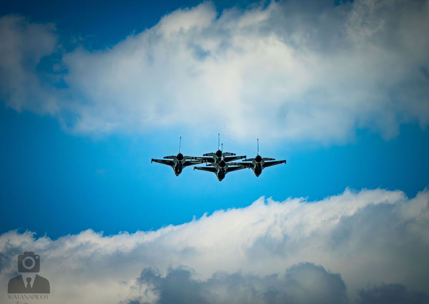 Two military jets flying in close formation against a bright blue sky with white clouds.