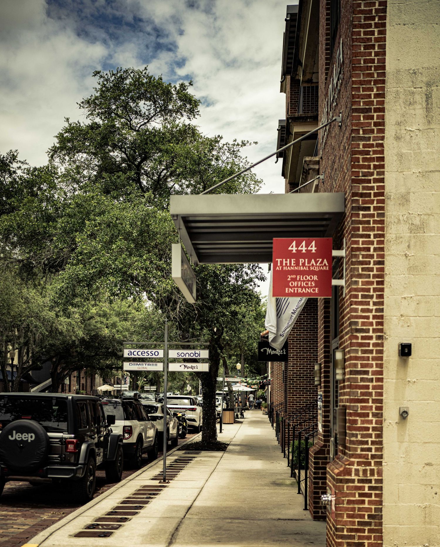 Historic brick building at 444 The Plaza with street-level awning entrance, lined with parked cars and lush trees.
