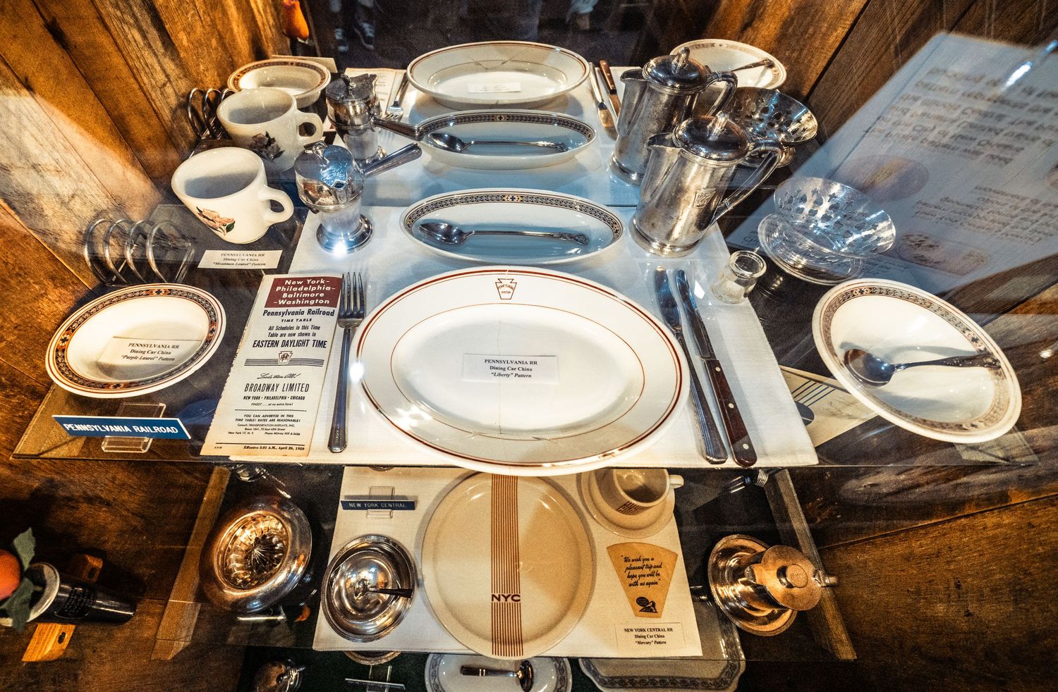 Row of antique white dinnerware and plates displayed on rustic wooden surfaces.