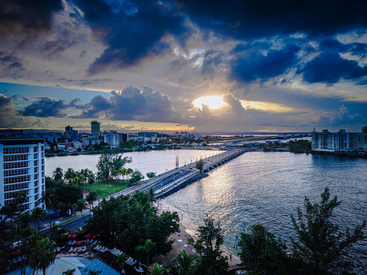 Panoramic aerial view of Waikiki Beach at sunset with dramatic clouds and city skyline along the coastline.