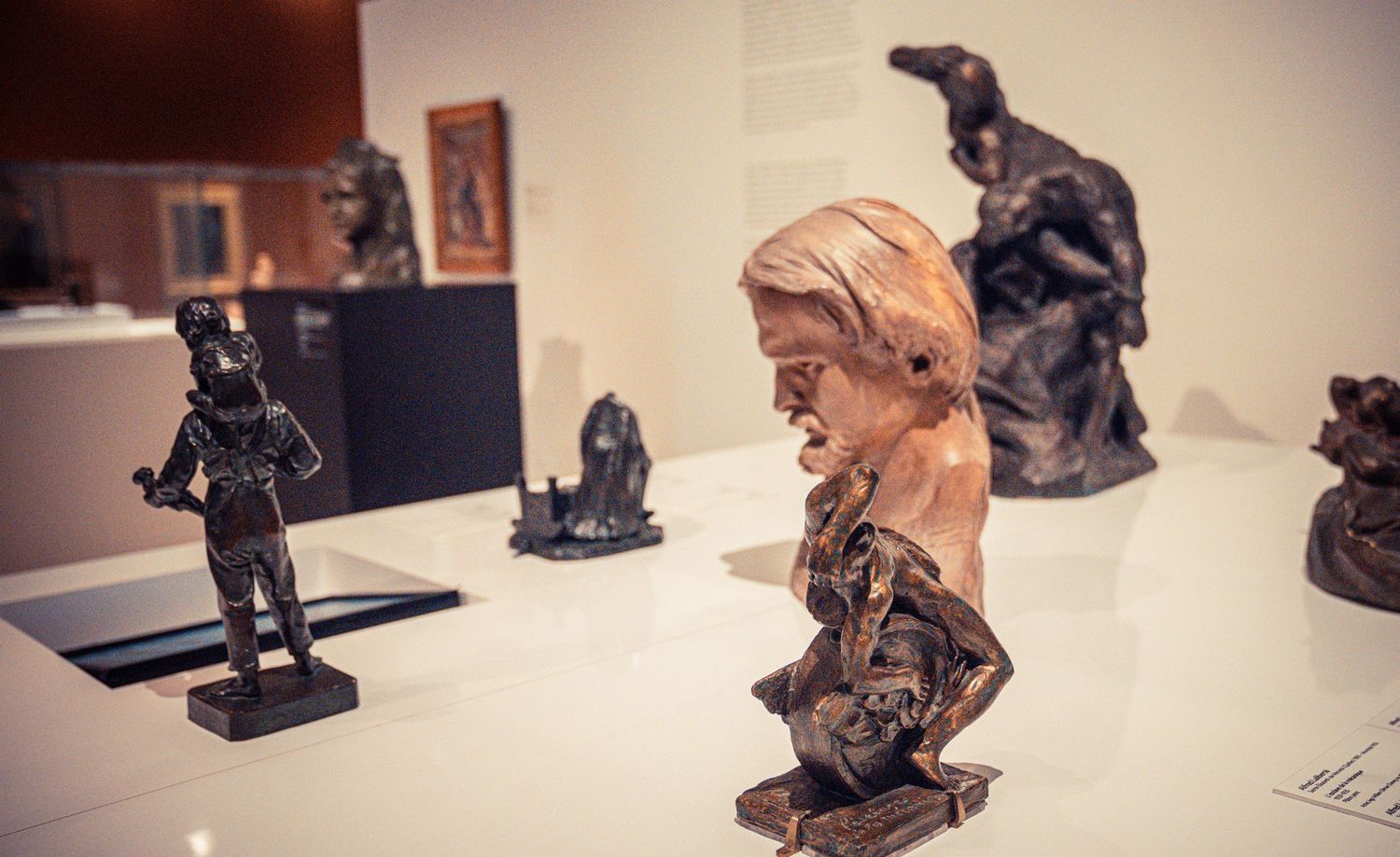 Collection of small bronze figurines and sculptures displayed on museum pedestals.