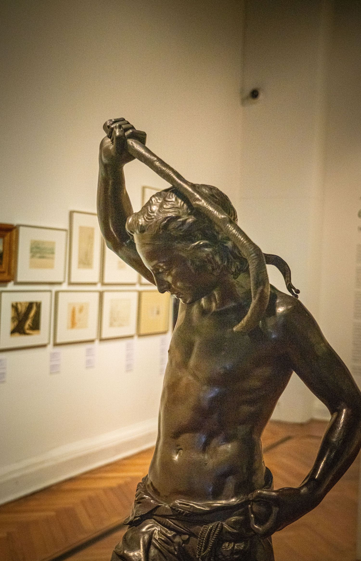 Bronze sculpture of a classical figure holding a raised object in an art gallery.