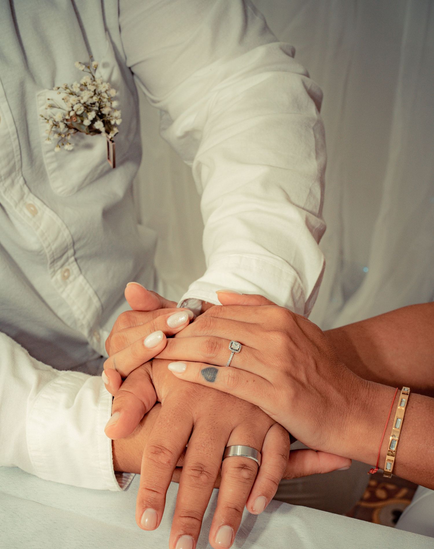 Close-up series of hands wearing wedding rings touching and overlapping in tender moments against white fabric background.