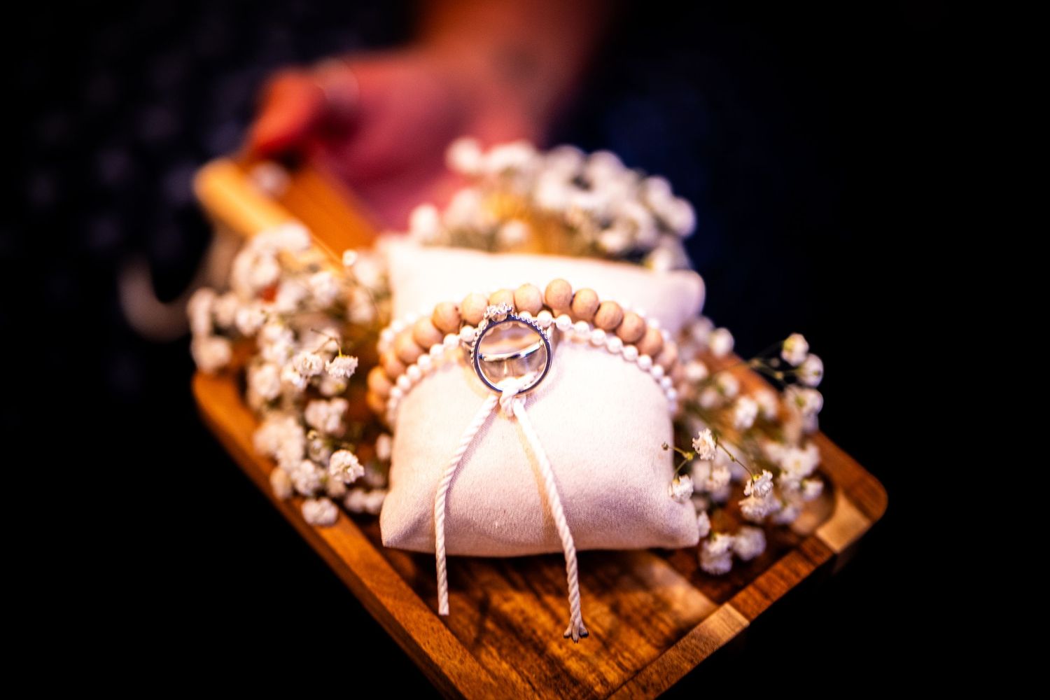 Wedding rings sparkle on a wooden surface surrounded by delicate white flowers and soft lighting.