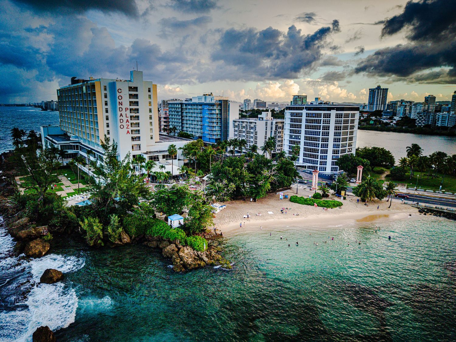 Coastal panorama of Hawaii showing luxury condominiums along the shoreline with crystal clear waters and rocky outcrops.
