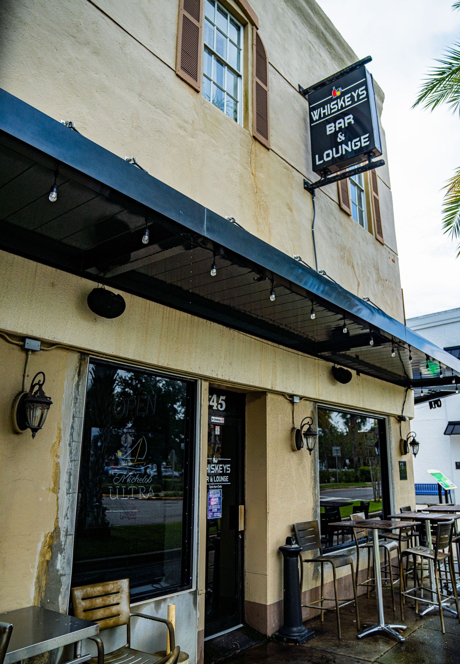 Exterior view of a beige building with black awnings and outdoor seating area.