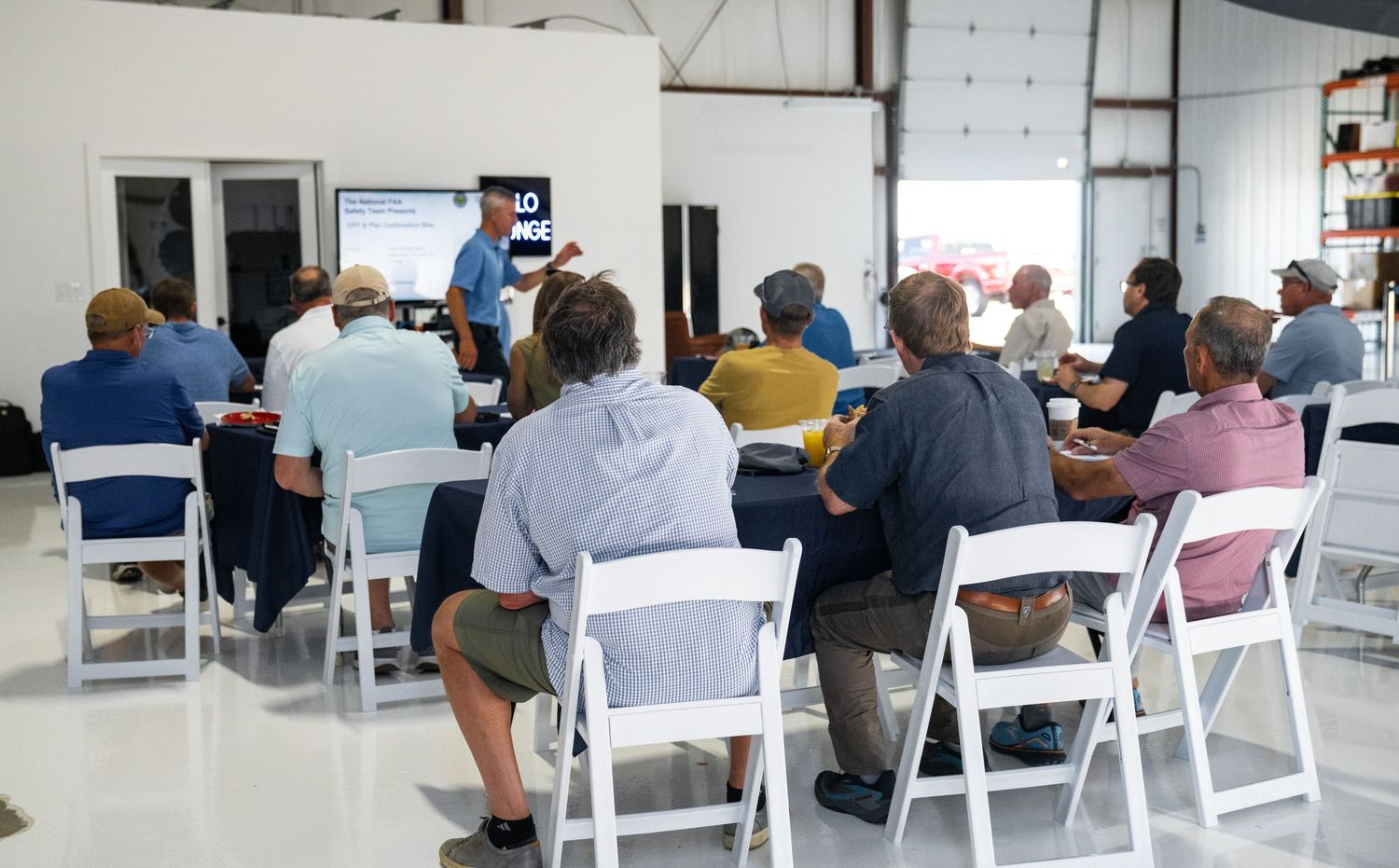 Wide view of a training session with white chairs arranged in rows inside an industrial building.