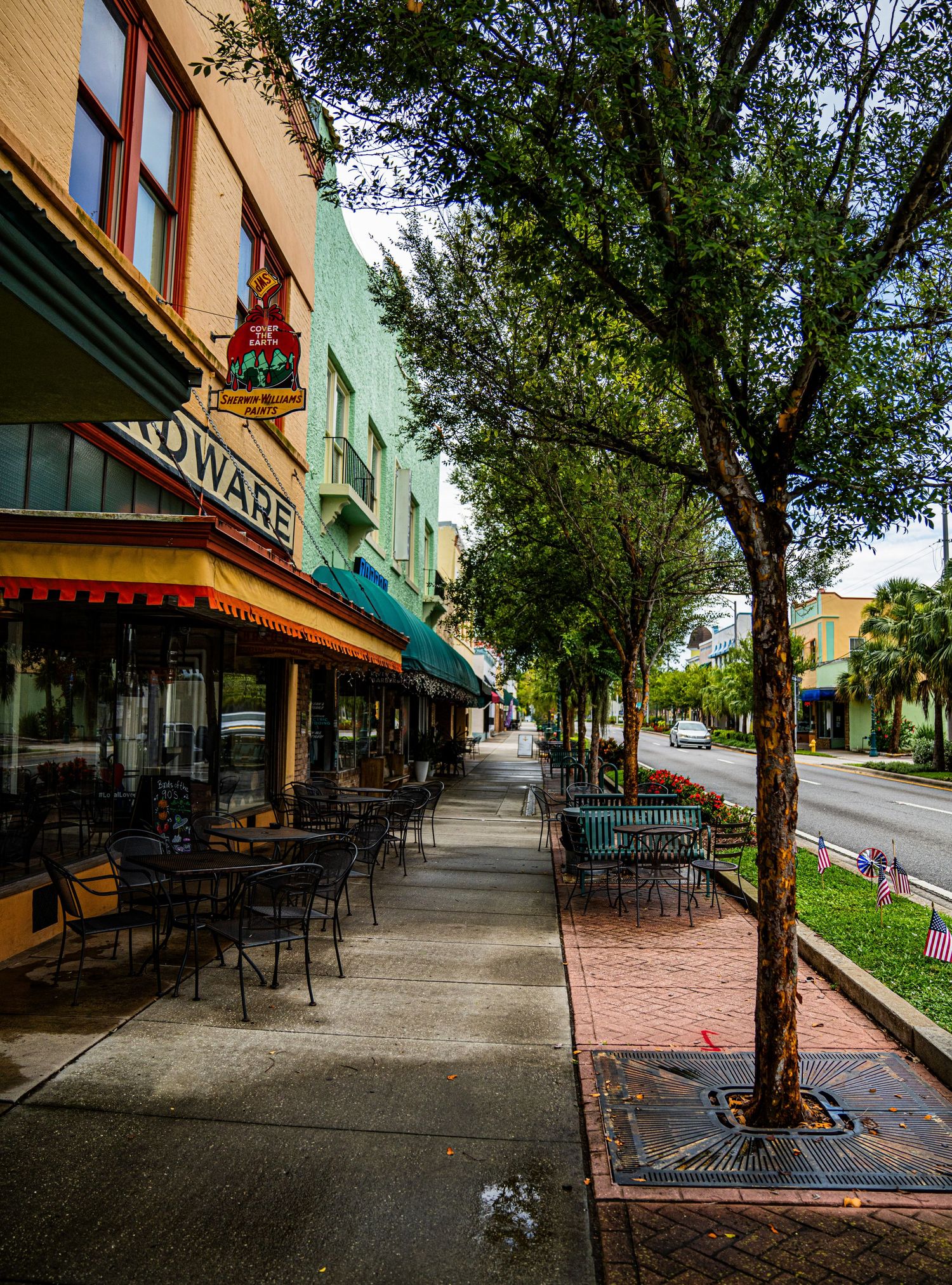 Historic downtown street with brick sidewalks, green awnings, and mature trees providing shade along storefronts.