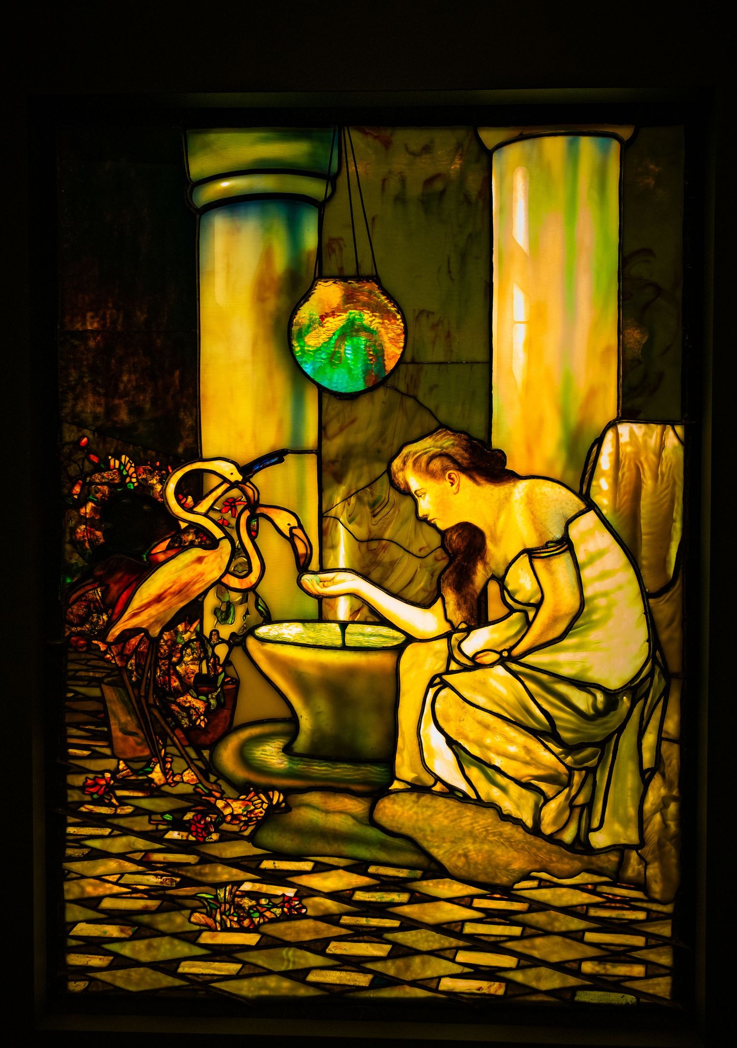 Stained glass artwork showing figures in flowing robes against a geometric patterned floor.