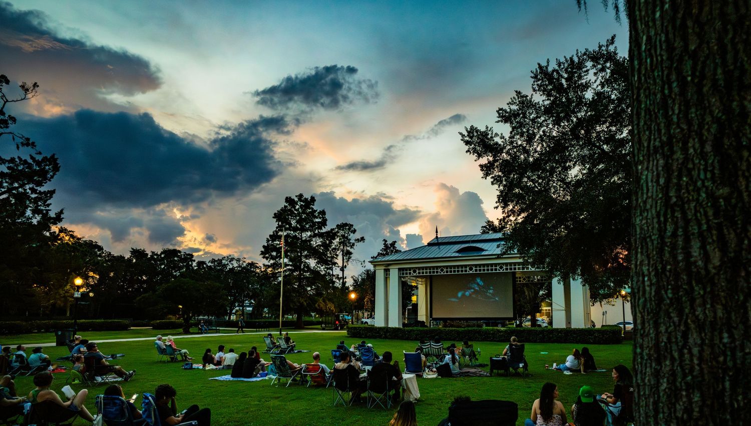 Sunset view of a historic park entrance with white columns and palm trees against a dramatic cloudy sky.