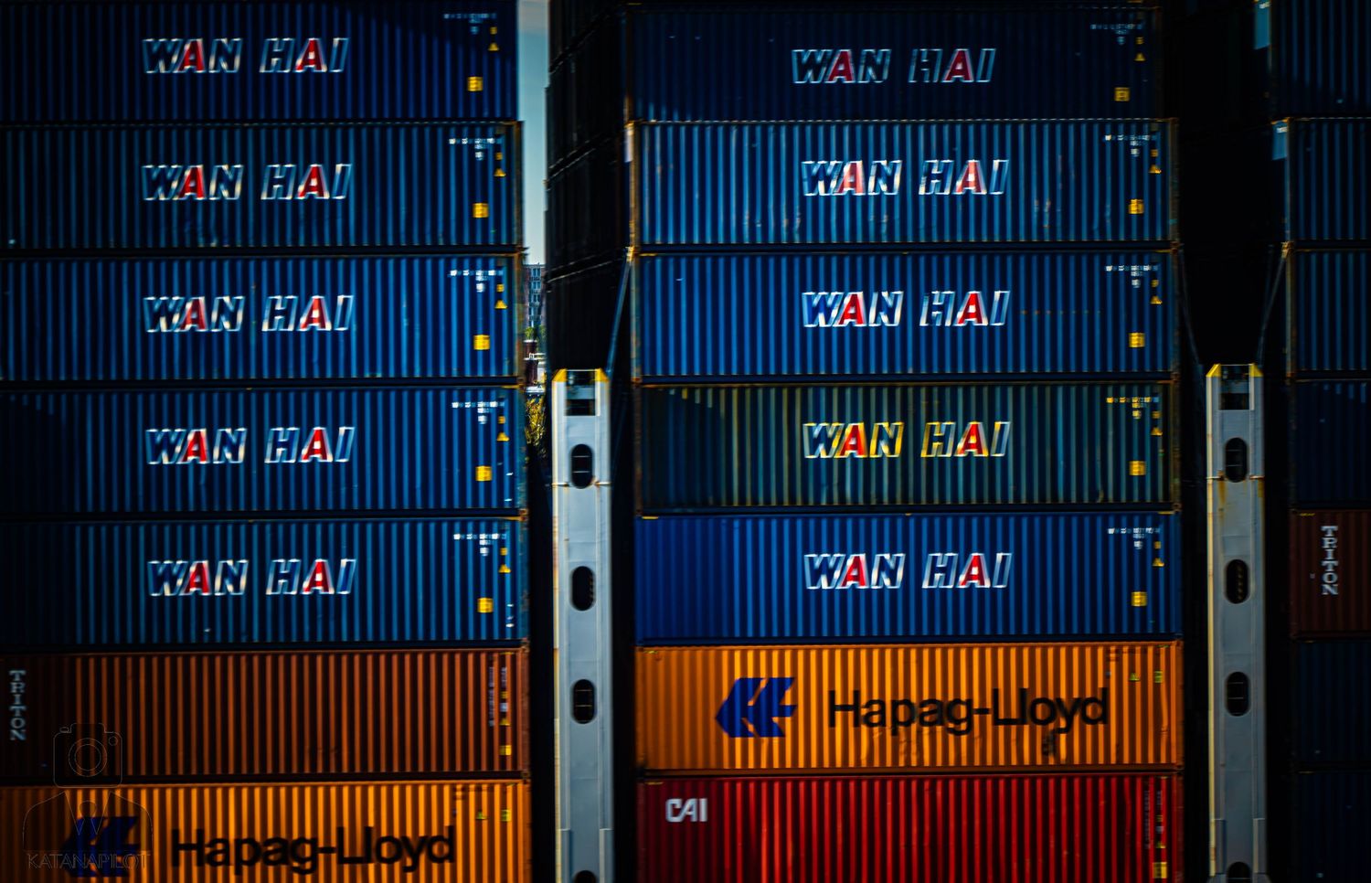 Stacked shipping containers with company logos arranged in rows at a port terminal.