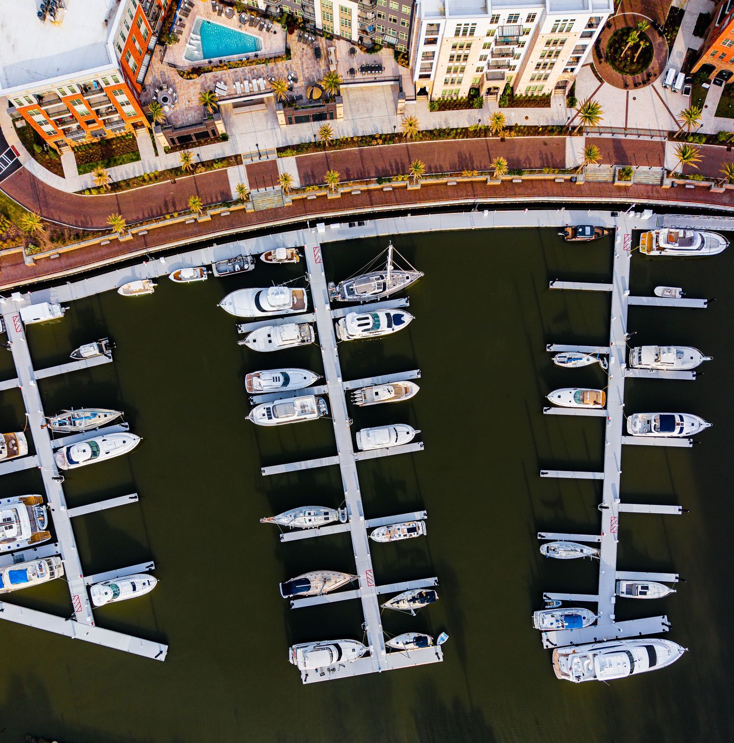 Aerial view of boats docked at a marina with white piers and docks creating geometric patterns in dark water.