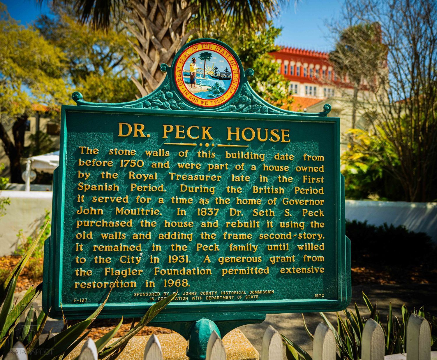 Historic green and gold Dr. Peck House historical marker sign with palm trees in background.