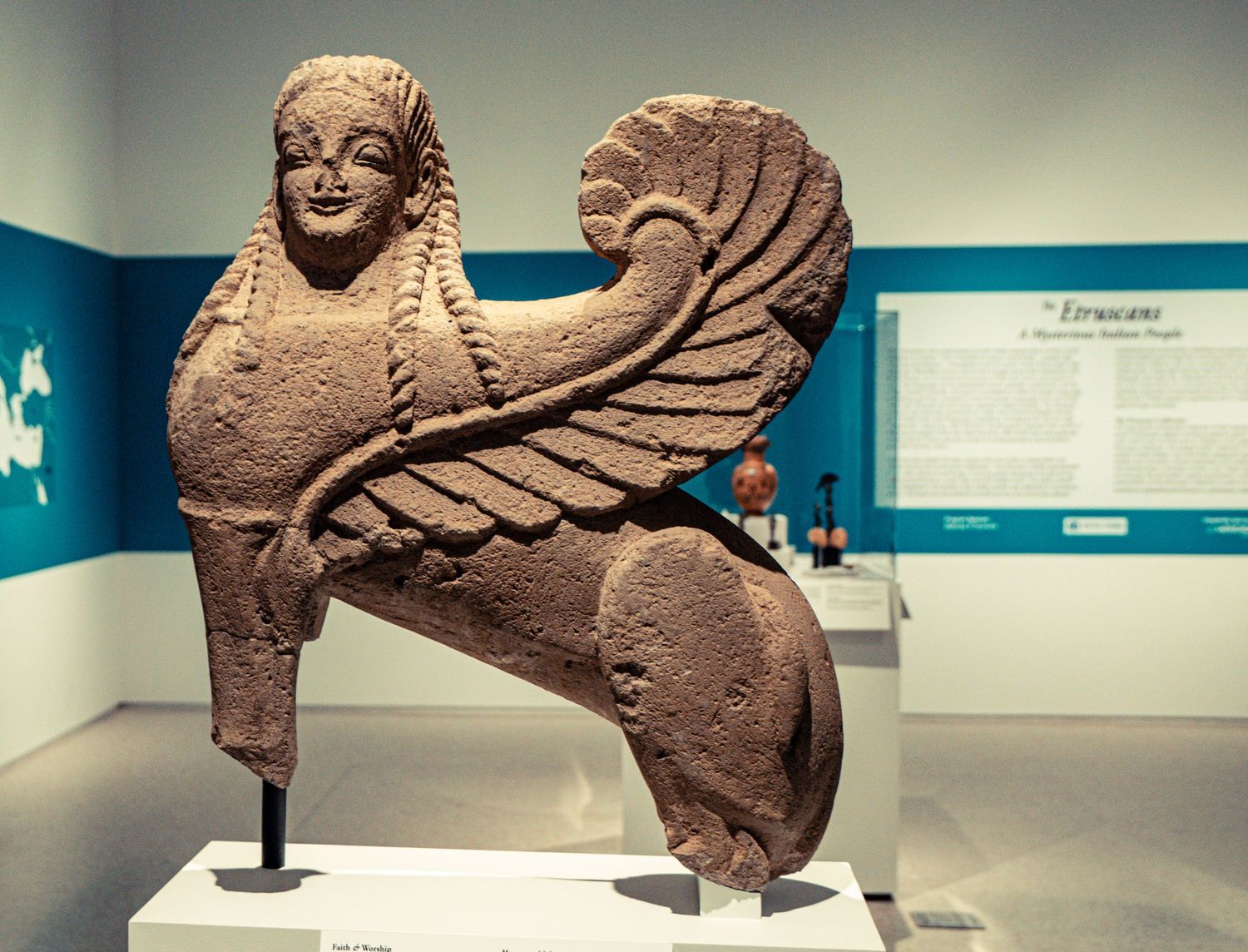 Ancient terracotta sculptures of mythical creatures displayed in museum exhibit cases with soft lighting.