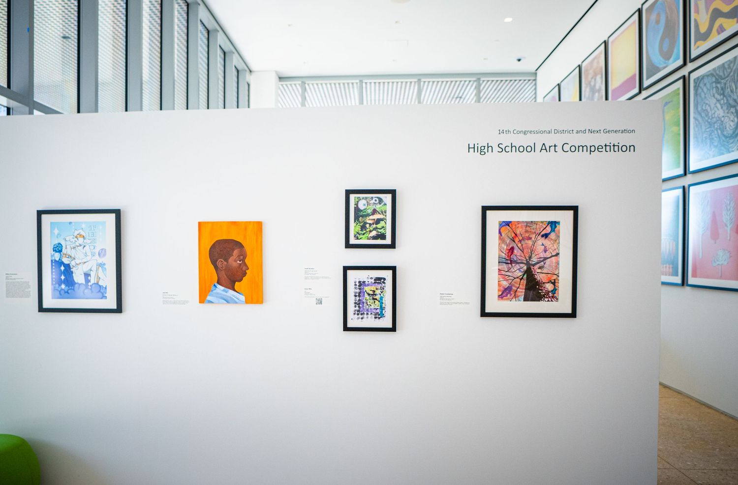 Art gallery wall displays framed artwork and student pieces in a bright hallway exhibition space.