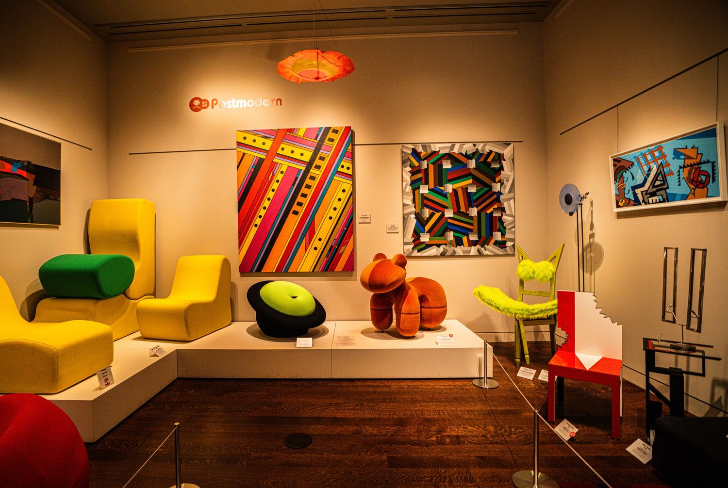 Modern art gallery space featuring colorful abstract paintings and retro-style furniture in yellow, green and orange tones.